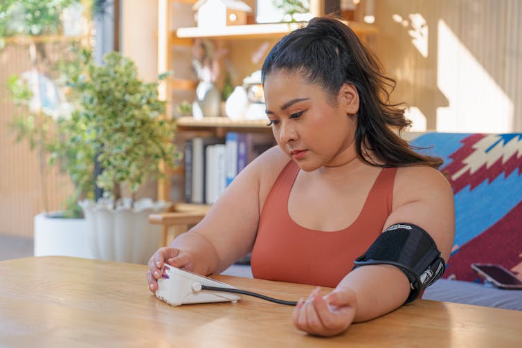 Woman using blood pressure meter to check her blood and heart rate pressure at home.