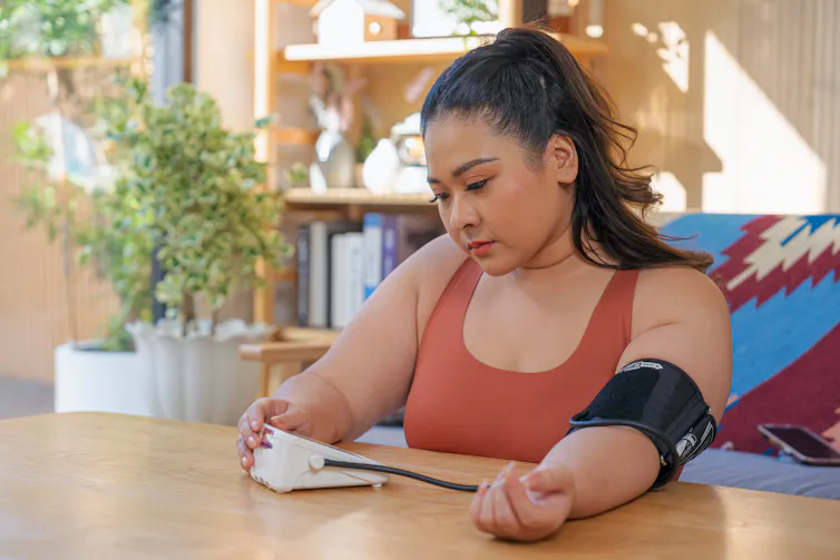 Woman using blood pressure meter to check her blood and heart rate pressure at home.