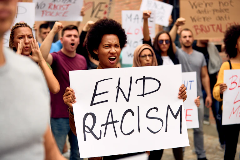 Woman in crowd of protestors holding sign saying 'END RACISM'