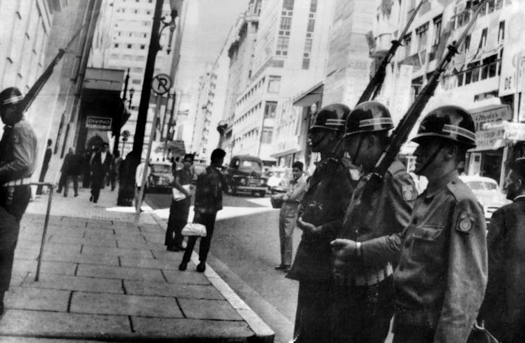 Black-and-white photo shows military officers lining a street in a big city.