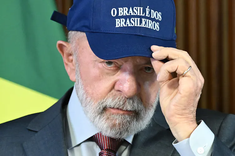 Man with a trim gray beard dons a cap emblazoned with a Portuguese phrase: 'O Brasil e de os brasileiros.'
