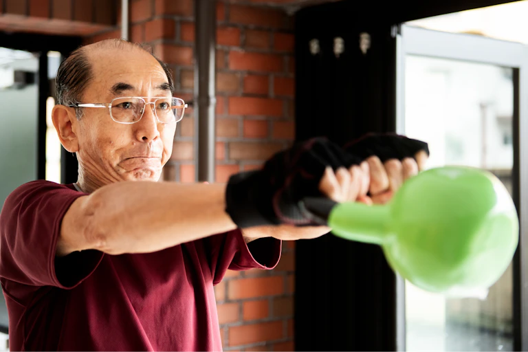 older man slightly grimaces as he swings a kettlebell out in front with arms parallel to the floor