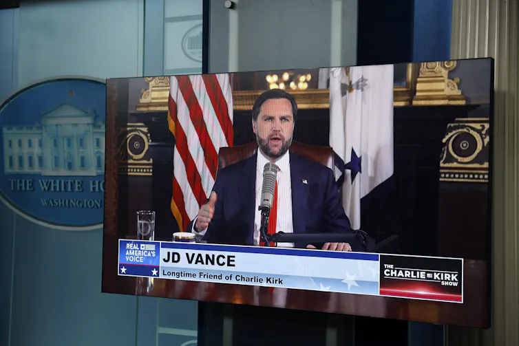 A TV screen projects footage of Vice President JD Vance in the White House Briefing Room.