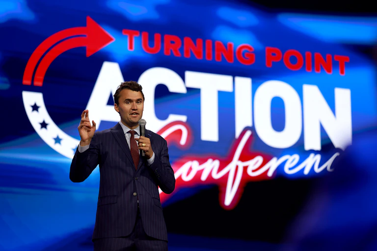 Young man in a tie speaks against a backdrop with the words 'Turning Point Action Conference.'