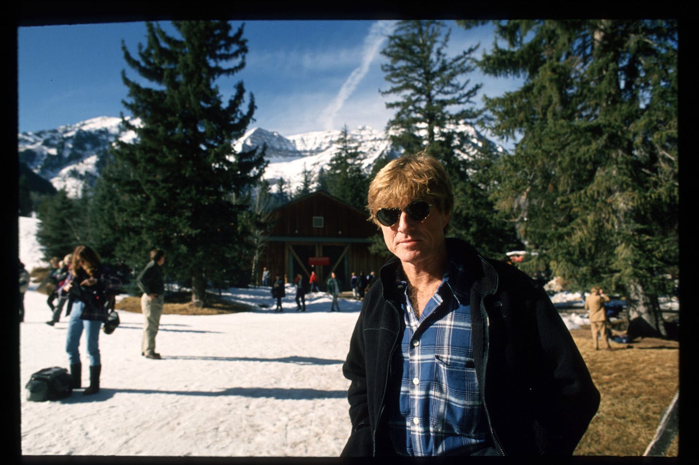 Redford poses for a photo in front of a snow capped mountain.