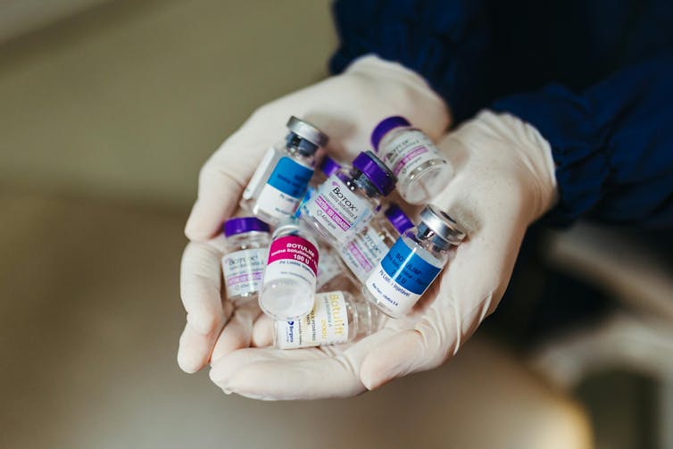 A pair of gloved hands holding numerous empty vials of botox