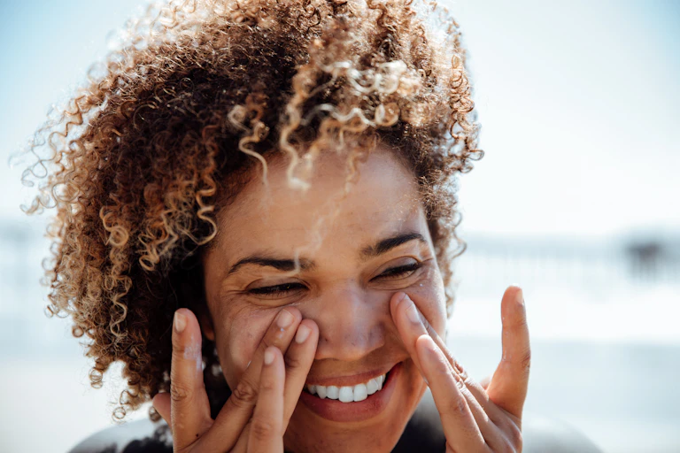 Woman with darker skin applying sunscreen to face with fingertips, at beach