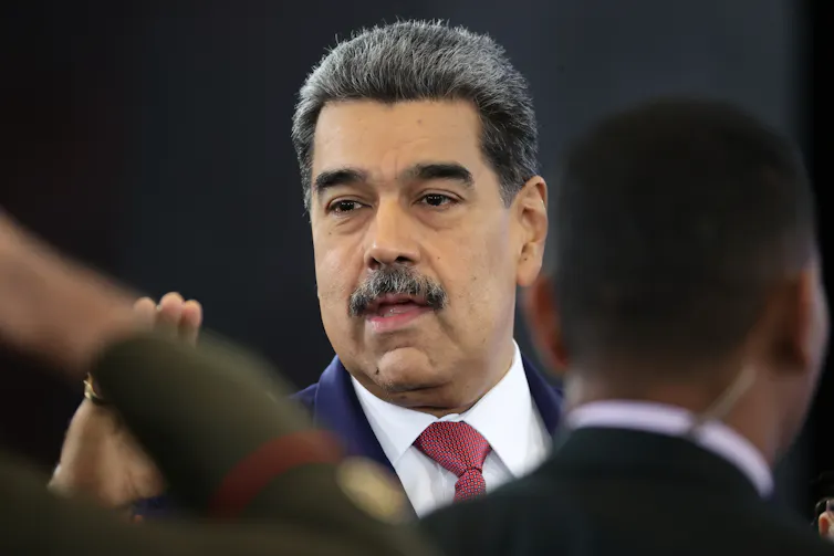 A man with a moustache speaks in a crowd.