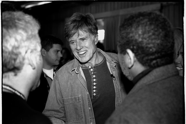 Redford sonríe mientras habla con la gente.