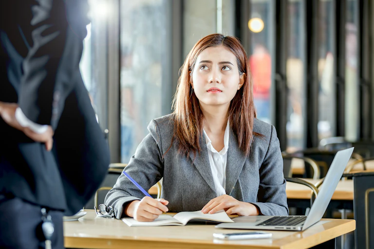 worried looking female office worker looking up at a threatening man standing over her