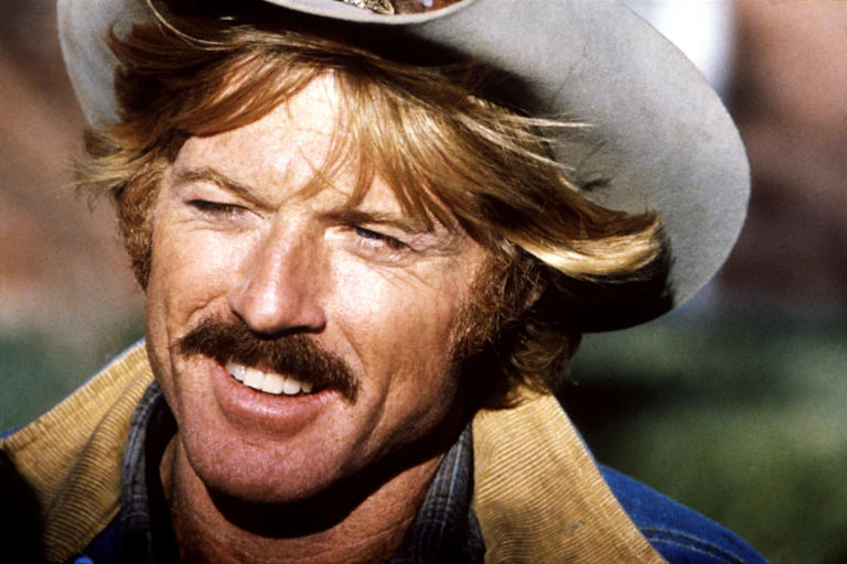 A handsome blond man sporting a moustache and a cowboy hat.