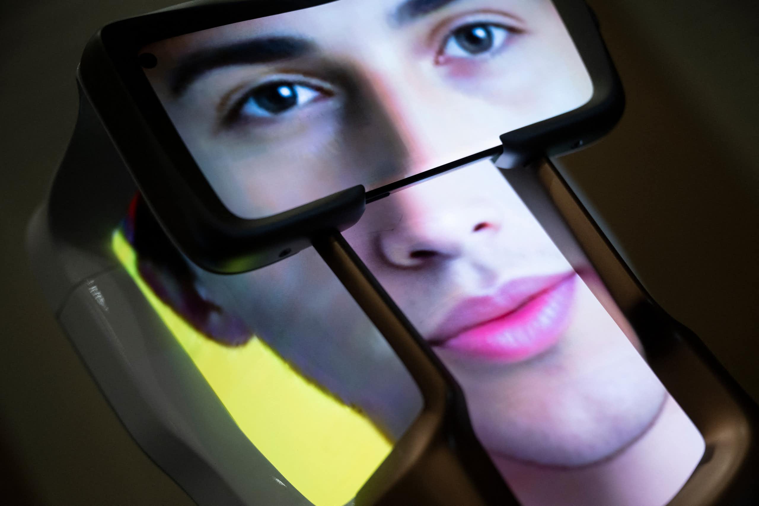 An image of what appears to be a human’s face is visible on the screens of what appears to be a three-dimensional device.