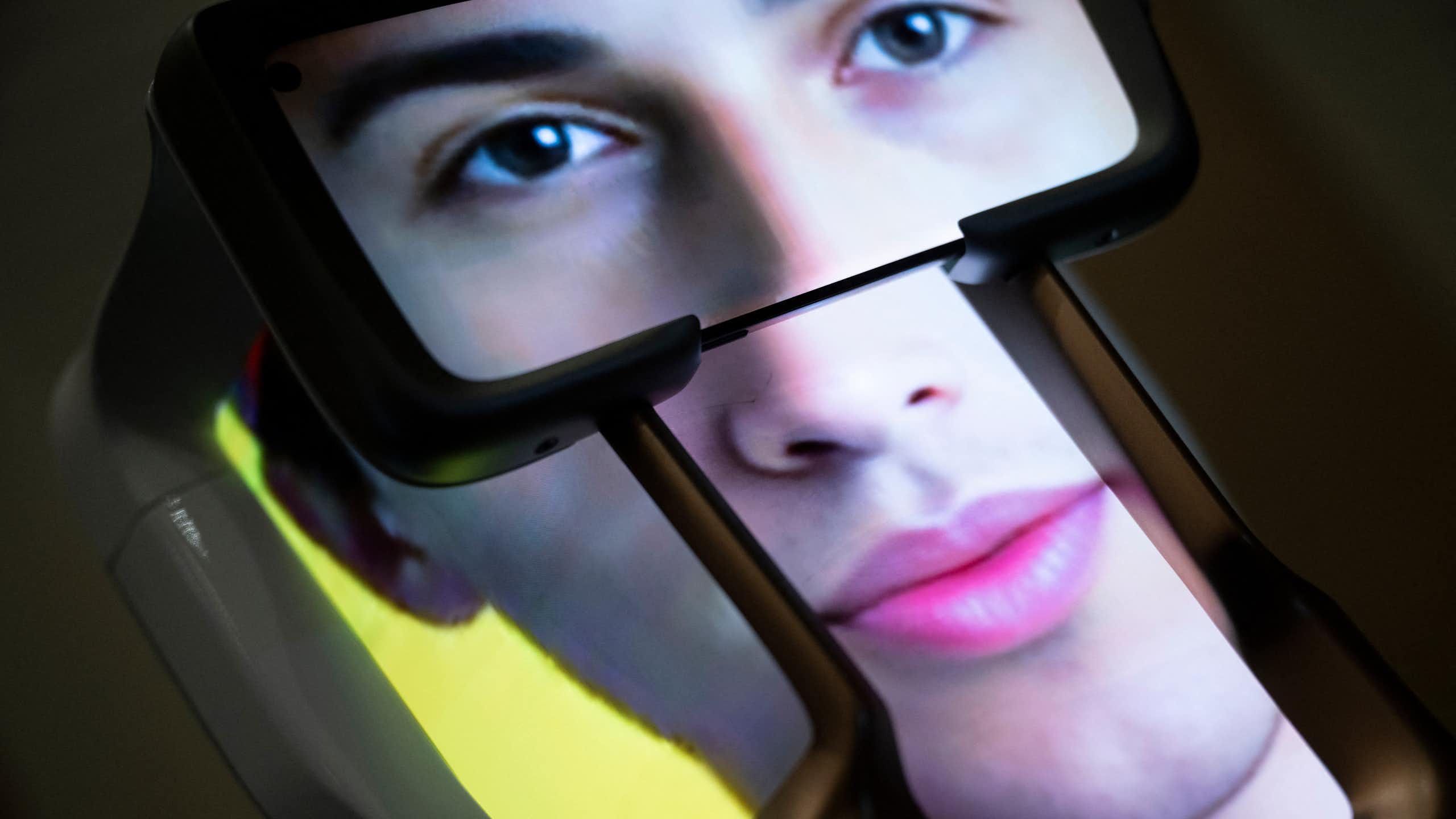 An image of what appears to be a human’s face is visible on the screens of what appears to be a three-dimensional device.