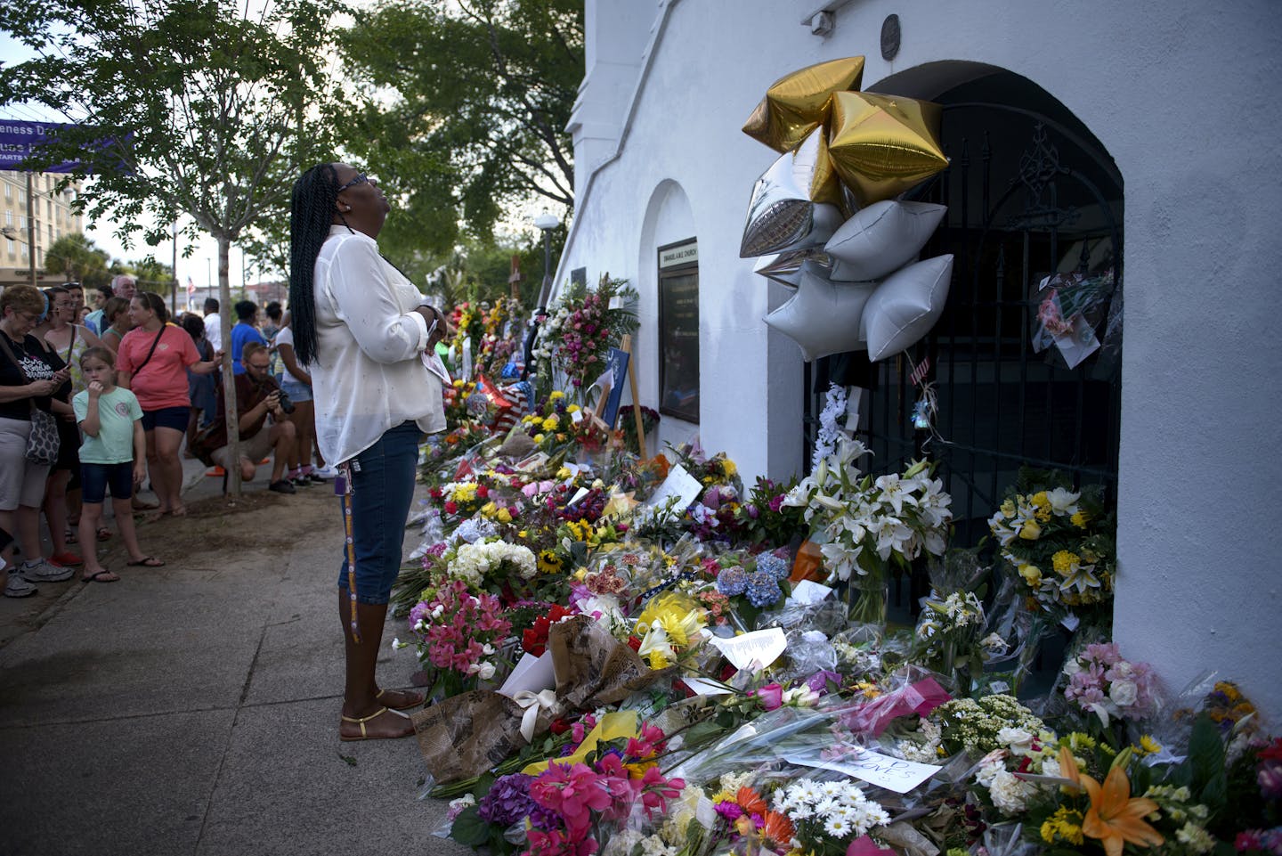 A woman crying at a memorial of many flowers outside a church.
