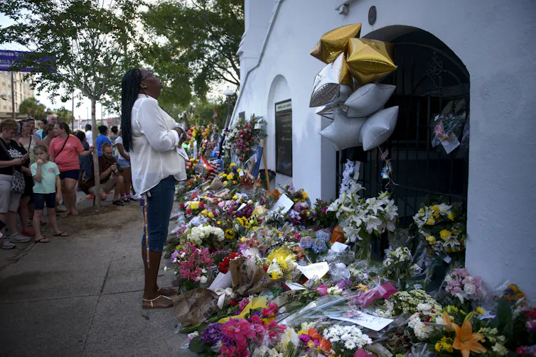 A woman crying at a memorial of many flowers outside a church.