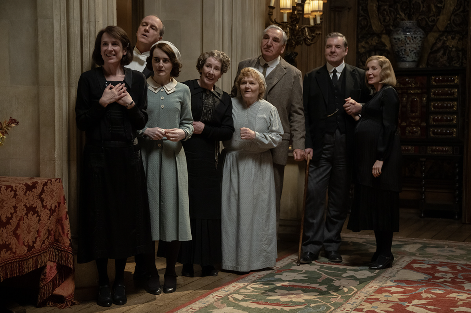 A group of servants standing looking expectant in a large grand Victorian castle.