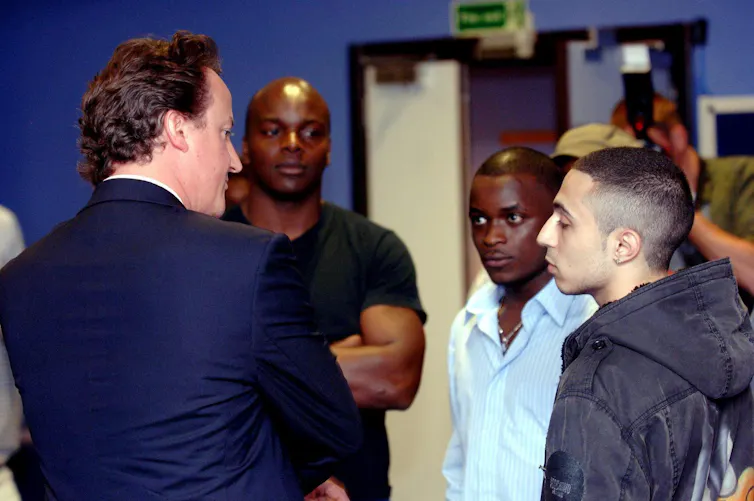 David Cameron talking to two young men.