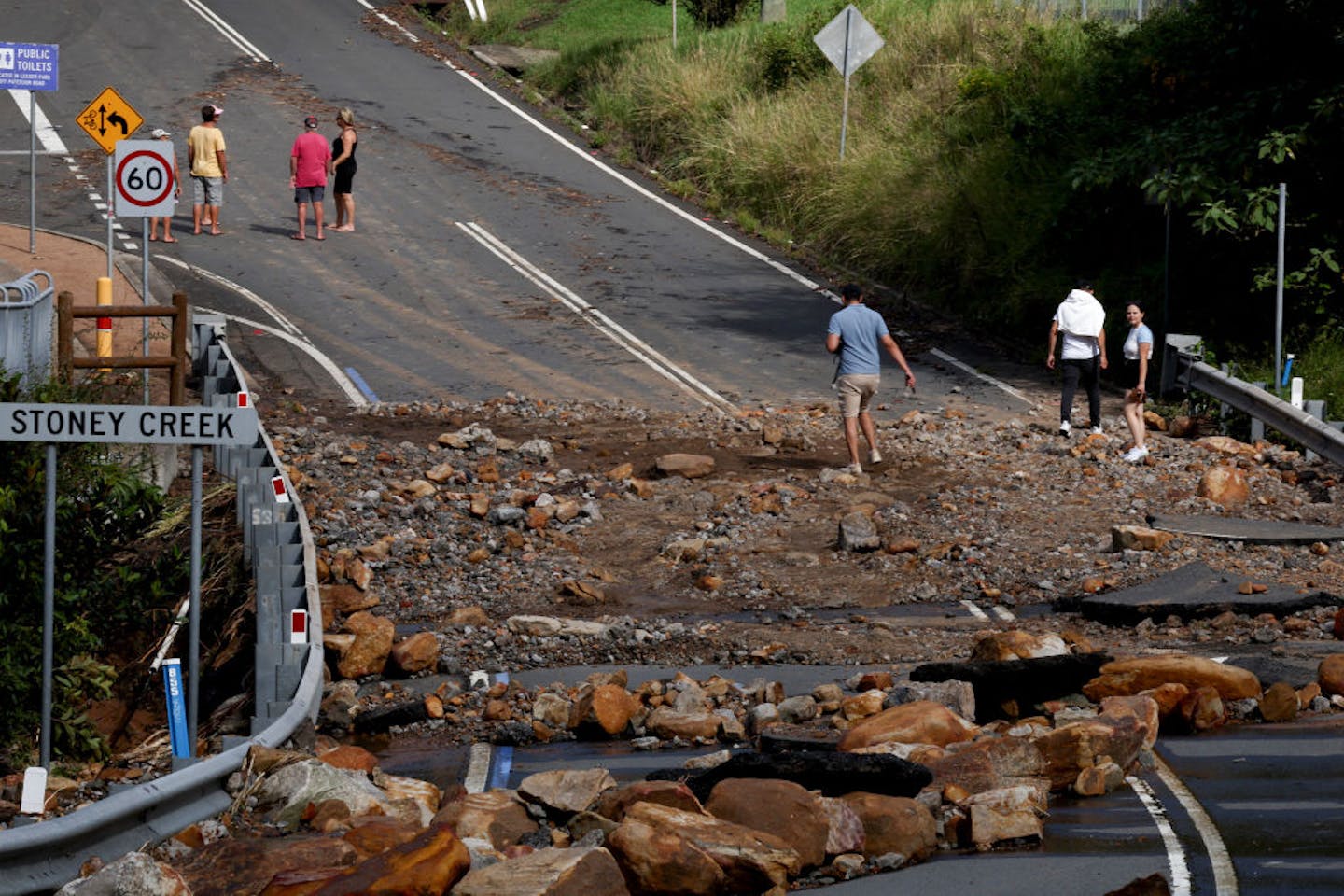 people walk and ride over a debris-covered road in aftermath of flooding.