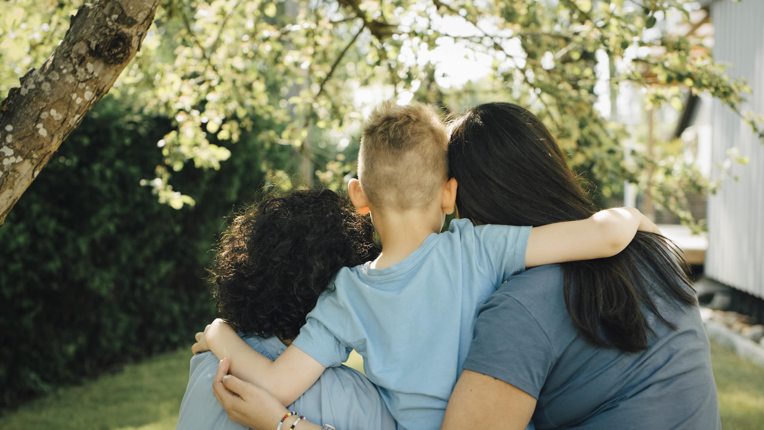 Two mums and their son, embracing, seen from the back