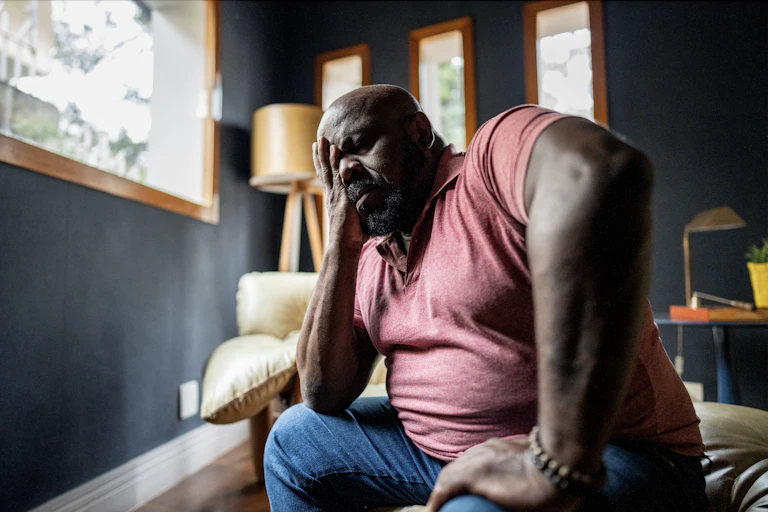 Man in pain sits on the edge of a couch
