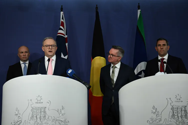 Four men stand on a podium in front of of flags