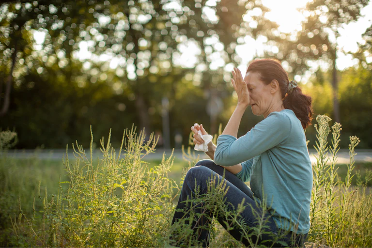 Woman sitting outdoors among grasses and blowing her nose