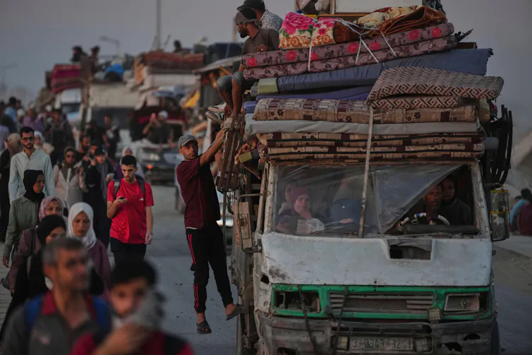 Palestinians walk or drive along a road with their belogings, some in trucks.