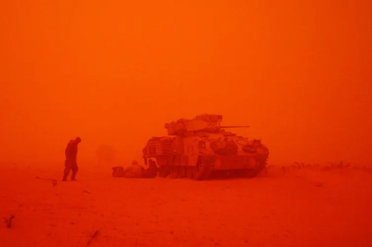 A man near a tank in a sandstorm that has turned the air red.