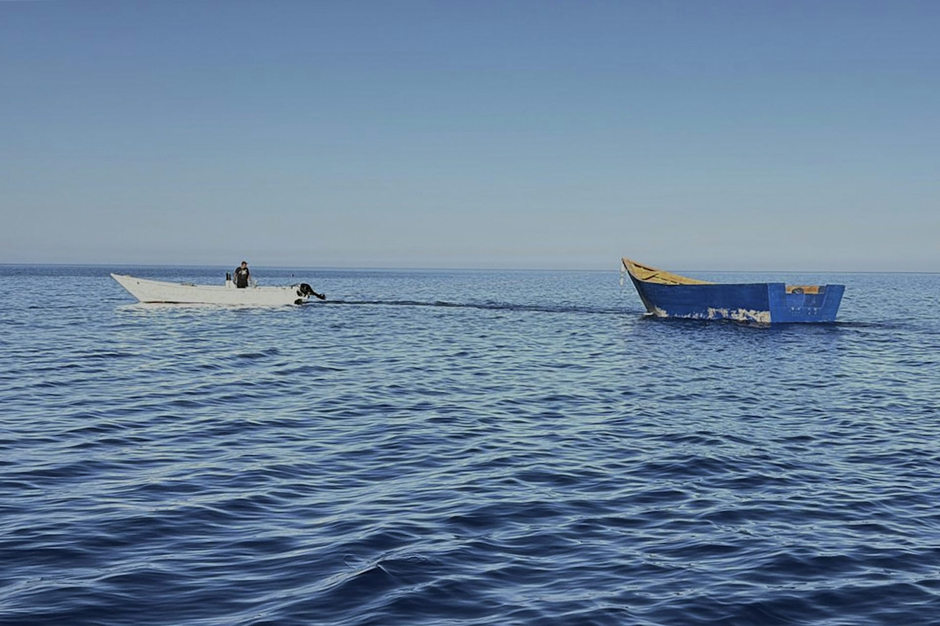 A white boat tows a larger blue boat.