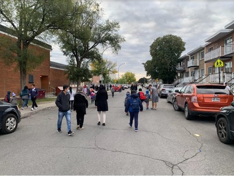 A street that has a school is closed off to motorists with children walking through it.