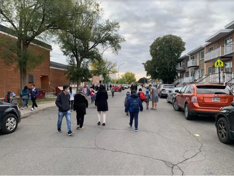 A street that has a school is closed off to motorists with children walking through it.