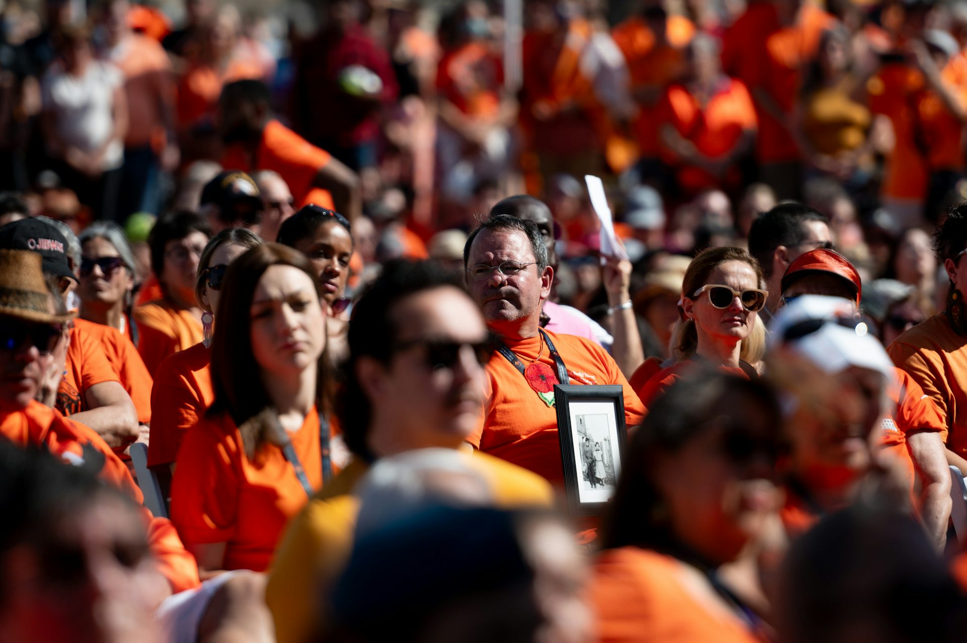 A crowd of people in orange shirts, one carrying a black and white framed photograph.