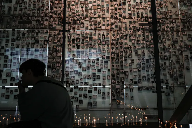 Hundreds of portraits of people appear on a wall.