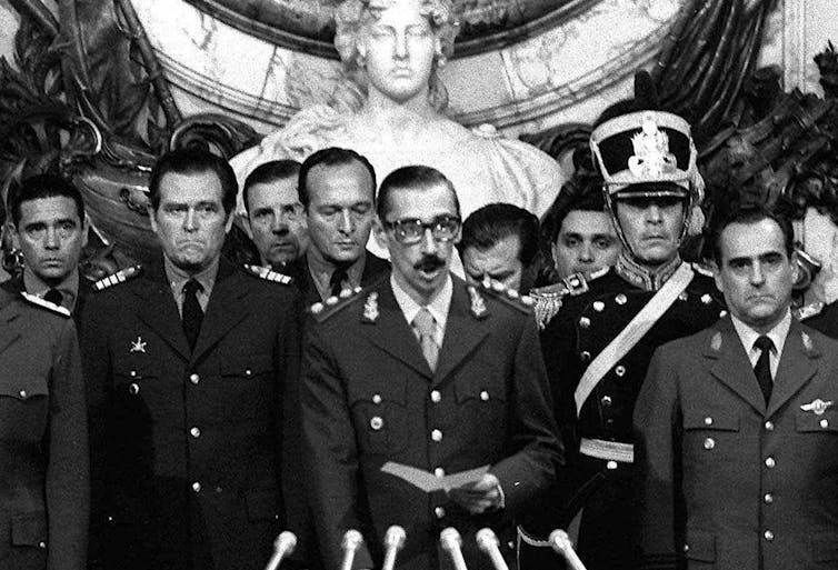 Several military men stand in front of microphones as one of them speaks.