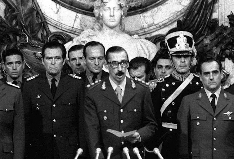 Several military men stand in front of microphones as one of them speaks.