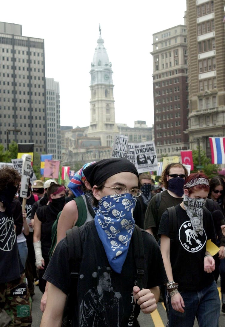 Young adults wearing black clothes and bandannas and holding protest signs