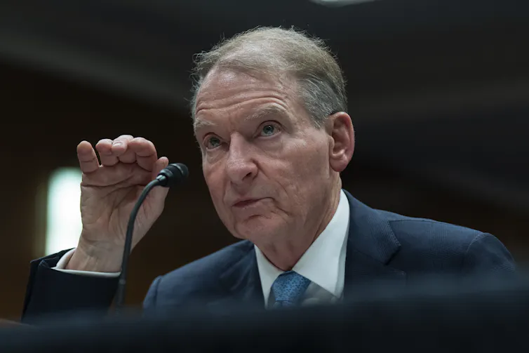 An older white man in a suit speaks into a microphone