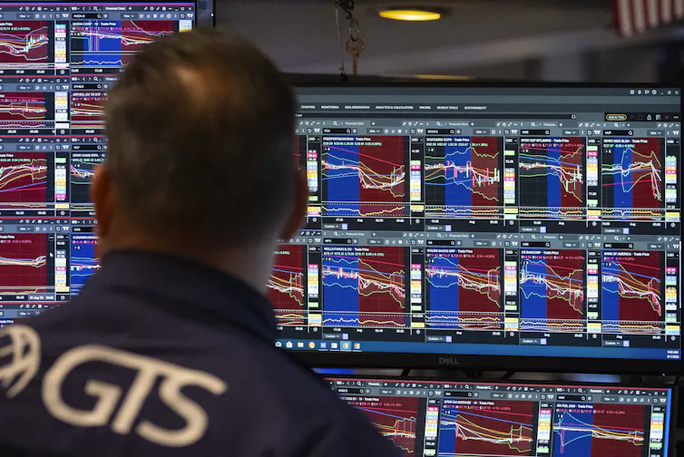 A man, seen from behind, looks at screens displaying stock exchange prices