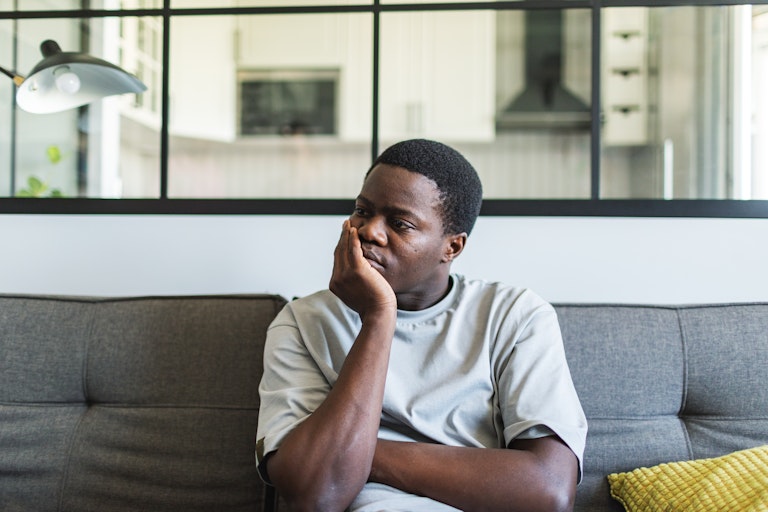 A young man sitting on a couch, looks despondent.