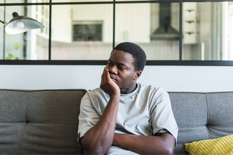A young man sitting on a couch, looks despondent.