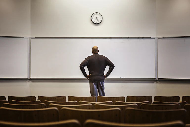 A man stands in front on an empty whiteboard in an empty lecture hall.