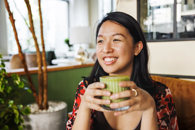 Women in a cafe smiles holding a matcha latte.