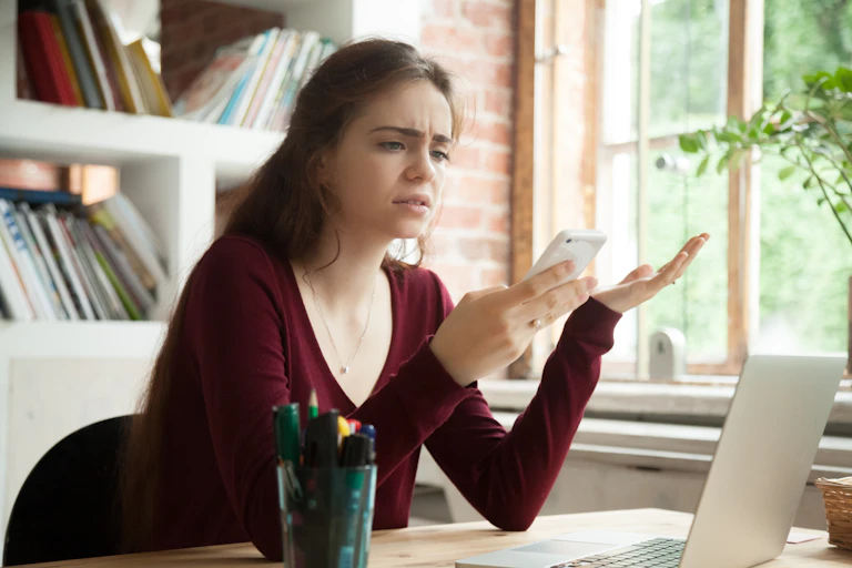 Una chica con gestos de frustración mirando su móvil.