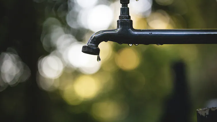 a drop of water falls out of a black faucet