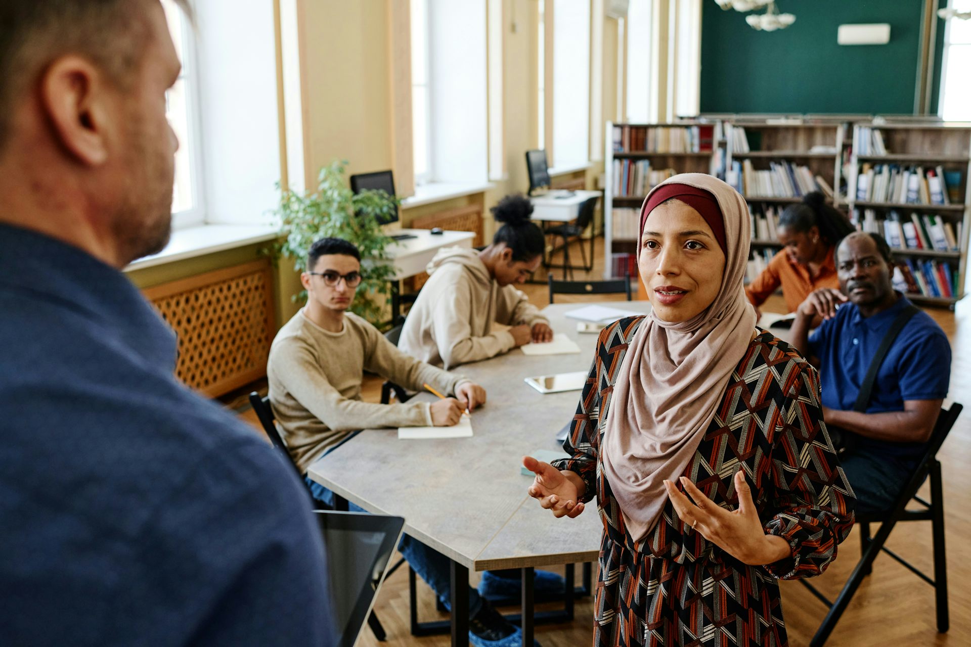 A class of adults having a discussion with a teacher who is at the head of class.