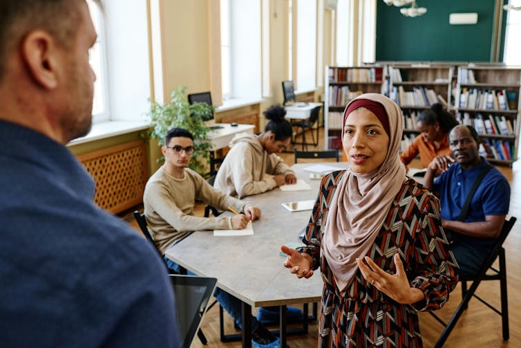 A class of adults having a discussion with a teacher who is at the head of class.