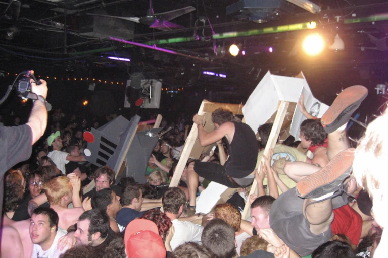Large crowd of mostly young men crowdsurfing and smashing cardboard robots