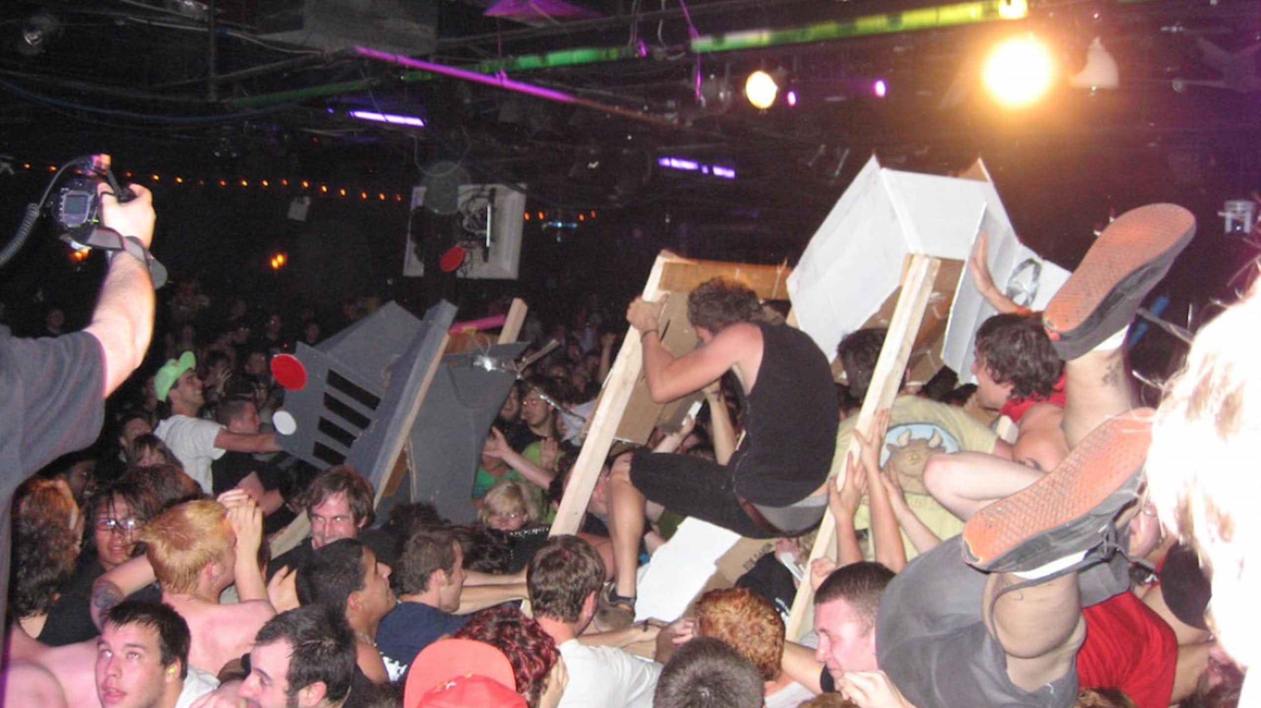 Large crowd of mostly young men crowdsurfing and smashing cardboard robots