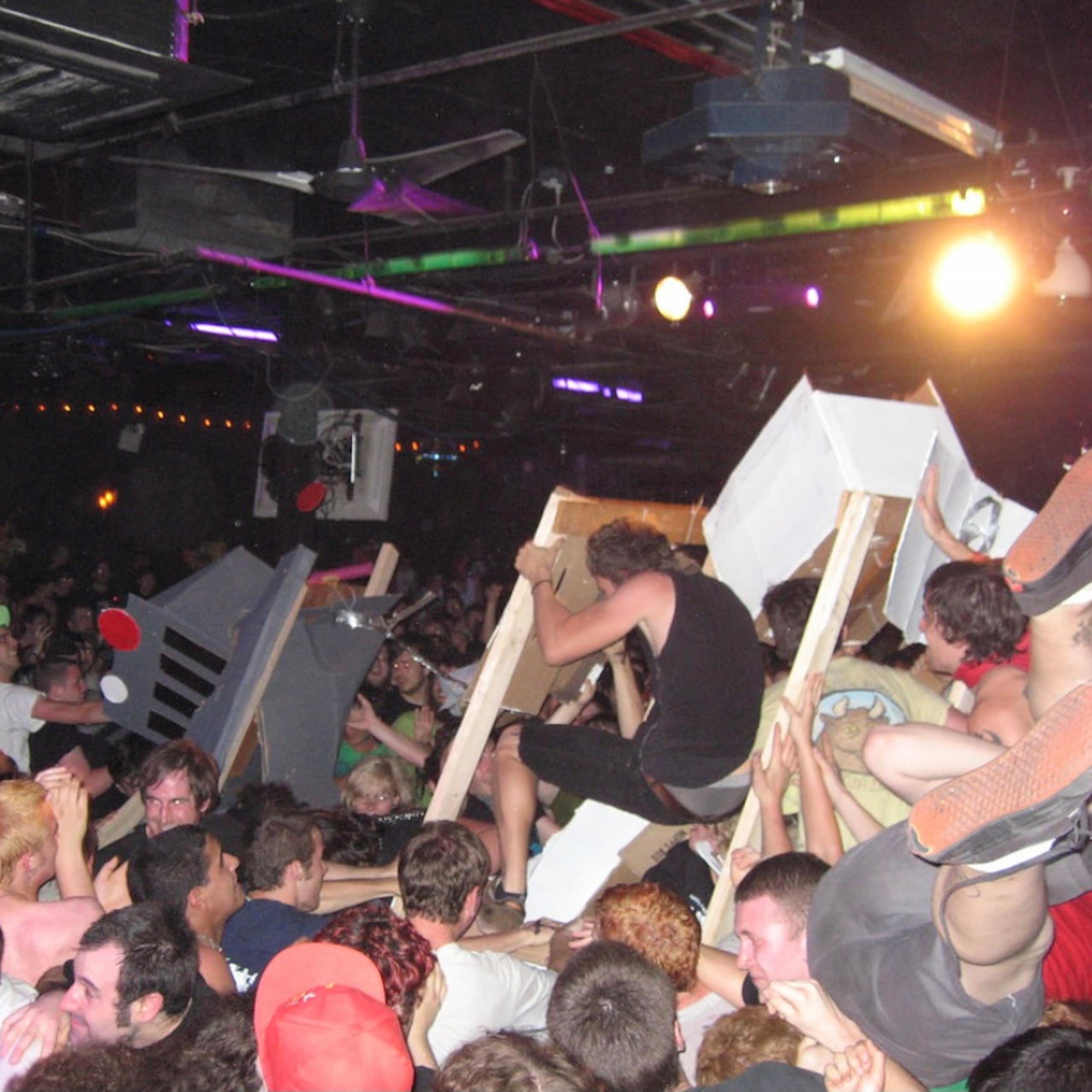 Large crowd of mostly young men crowdsurfing and smashing cardboard robots