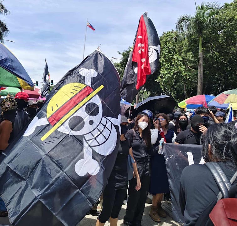 Una gran bandera con cráneo y esponjas mutuas está rodeada de personas.
